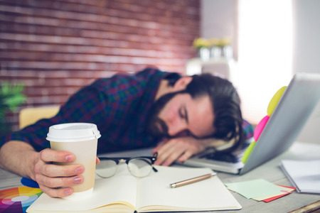 45537740 - tired creative editor holding disposable cup while sleeping on office desk